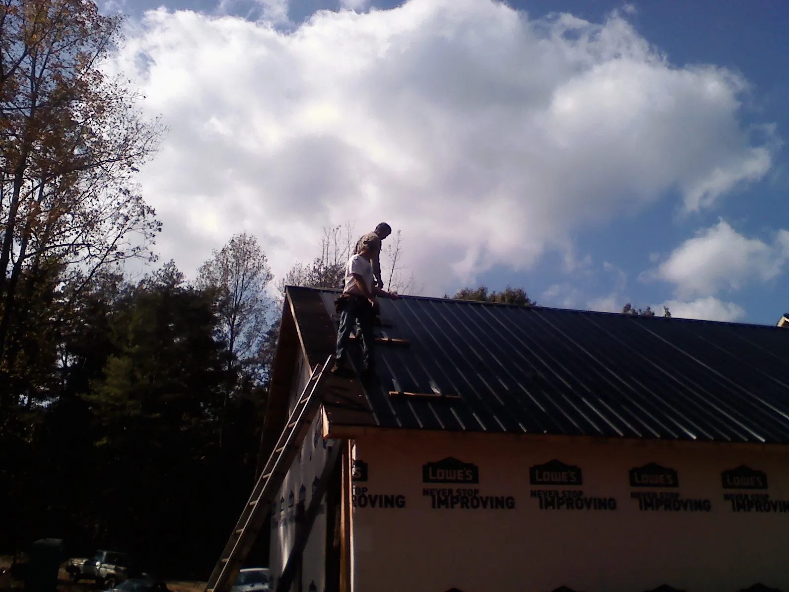 Roofer fastening dark metal panels high against a cloudy sky, from a Roof Inspection job in Geneva