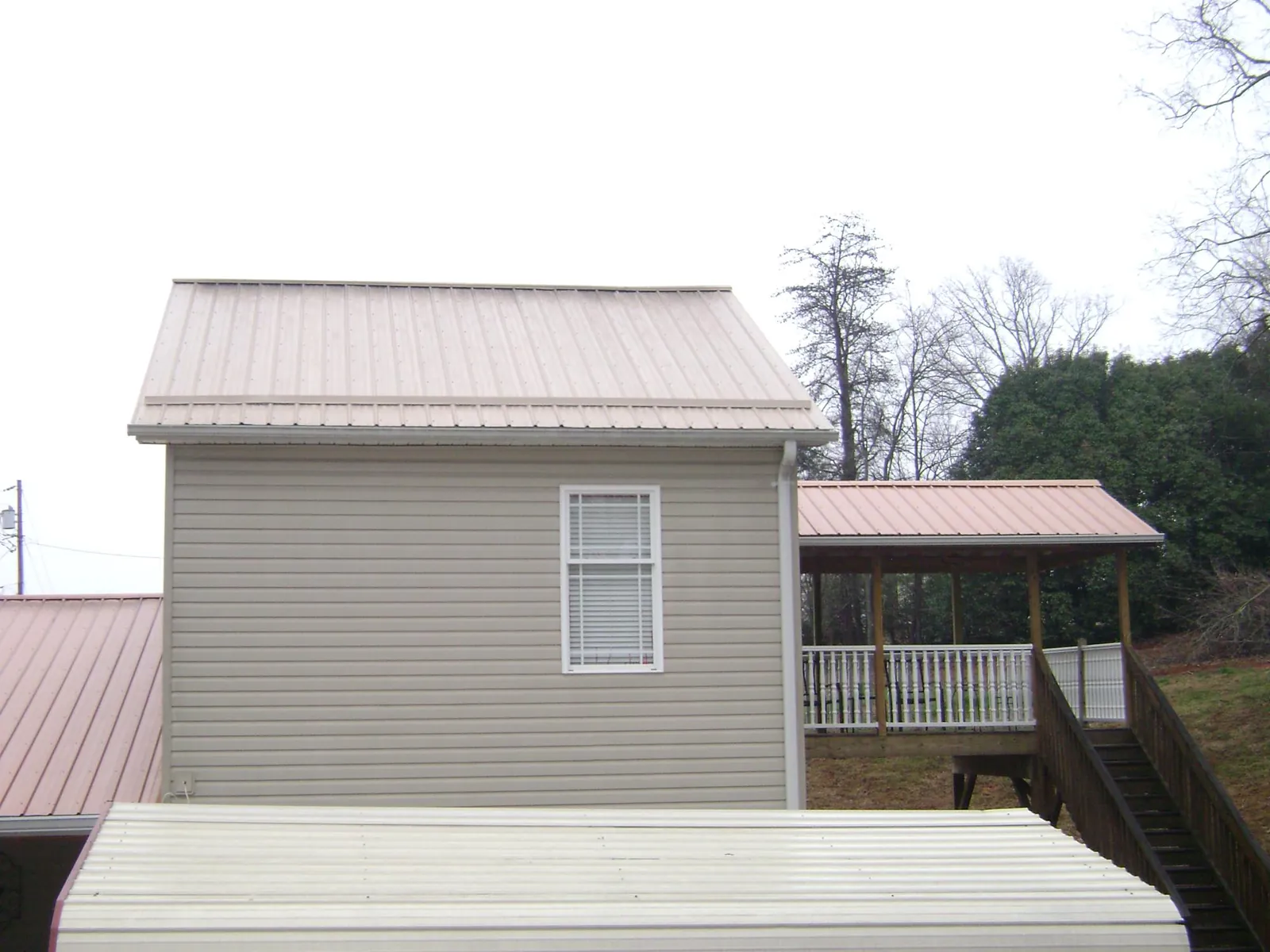 Tan metal roofs on a two story addition and attached porch, from a Roof Replacement job in Geneva